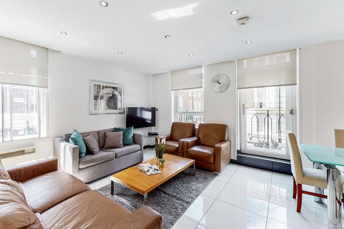 A modern living room with a sofa, coffee table, and chairs, a flat-screen TV, and a dining area with a glass table.
