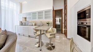 A modern kitchen with a central island, a dining area with two chairs, and a built-in oven. - Gloucester Place (London)