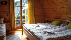A wooden cabin bedroom with a bed, a nightstand, a lamp, and a window with curtains.