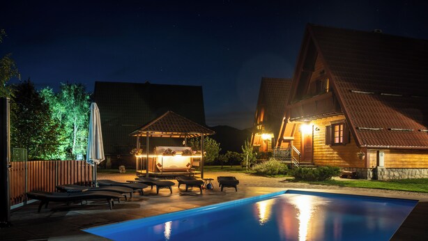 A pool area with lounge chairs and a gazebo, surrounded by wooden buildings with warm lighting.