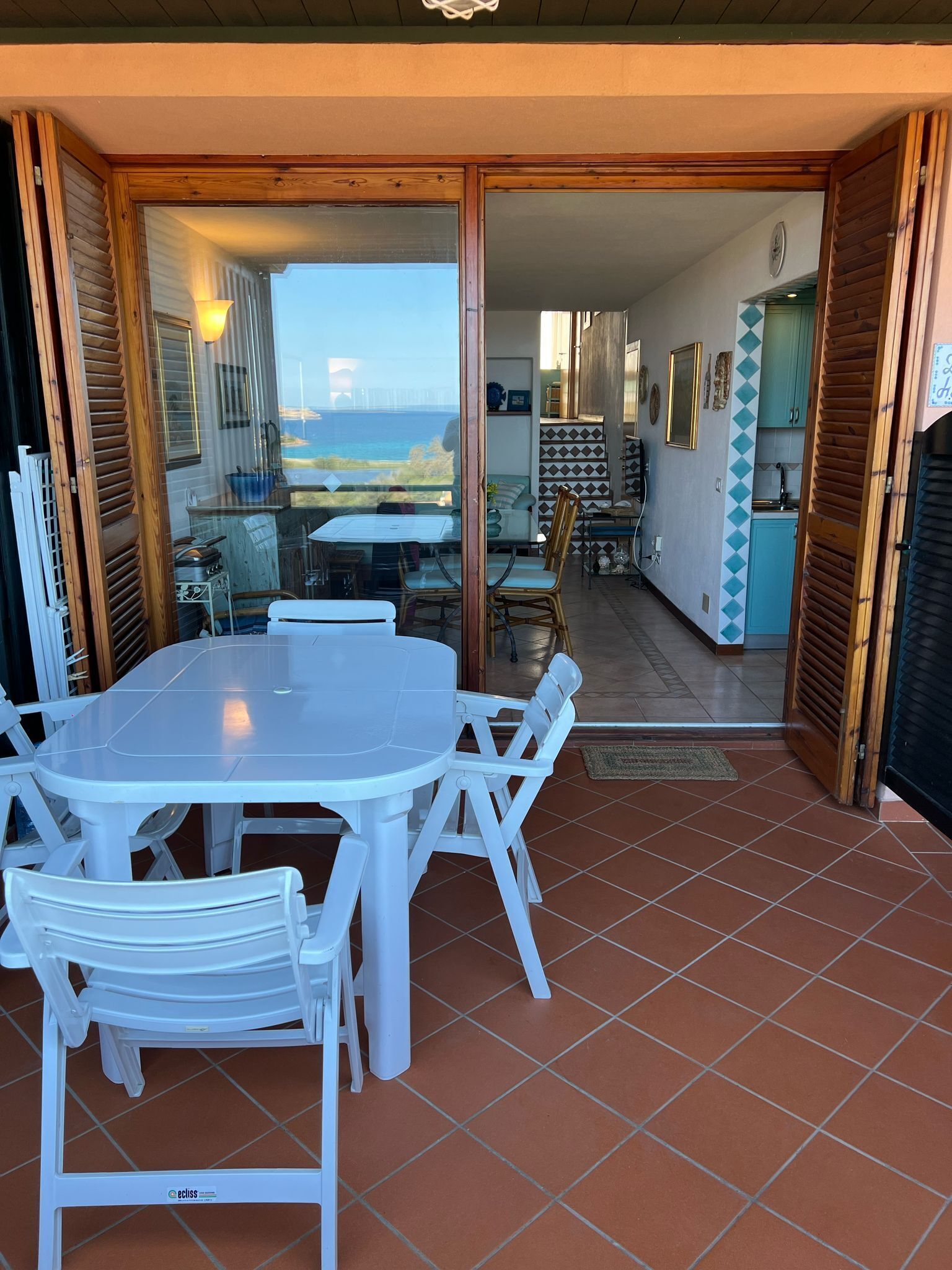 Un coin repas avec une table et des chaises blanches, une cuisine en arrière-plan et une vue sur la mer.