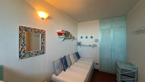 Ein Schlafzimmer mit einem Bett, Nachttisch, Regalen mit Büchern und Dekoration, einem Kleiderschrank und einem Spiegel mit Mosaikrahmen.