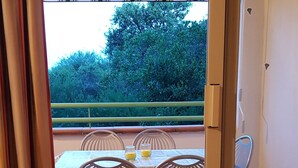 Une pièce dotée d’une porte-fenêtre coulissante donnant sur un patio extérieur avec une table et des chaises, une vue sur la verdure et un sol carrelé.