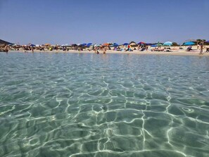 A beach with clear water, umbrellas, and people. - Accogliente casa vacanze a pochi passi dal centro e pochi minuti dalle spiagge (Villasimius)
