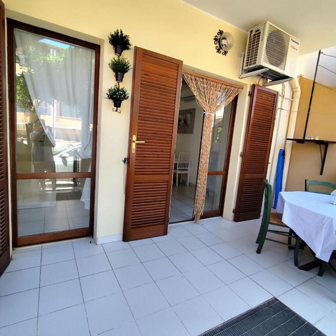 A room with a sliding glass door, a wooden door, a small table with a white tablecloth, and an air conditioning unit mounted on the wall.