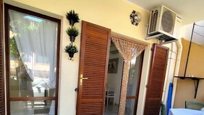 Une pièce dotée d’une porte-fenêtre coulissante, d’une porte en bois, d’une petite table recouverte d’une nappe blanche et d’un climatiseur fixé au mur.