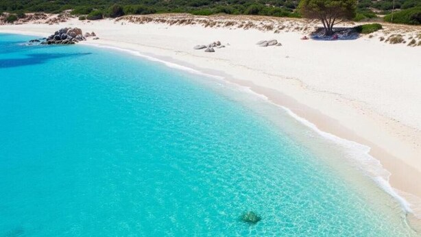 Une plage à l’eau turquoise et limpide, au sable blanc, parsemée de rochers.