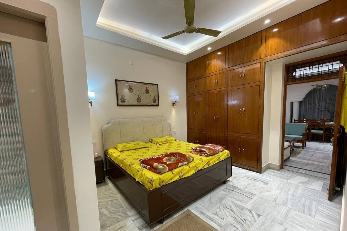 Un dormitorio con cama, armario, ventilador de techo y una zona de comedor al fondo.