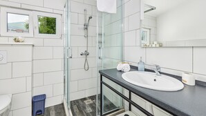 Ein modernes Badezimmer mit Duschkabine aus Glas, einem weißen Waschbecken und einem großen Spiegel.