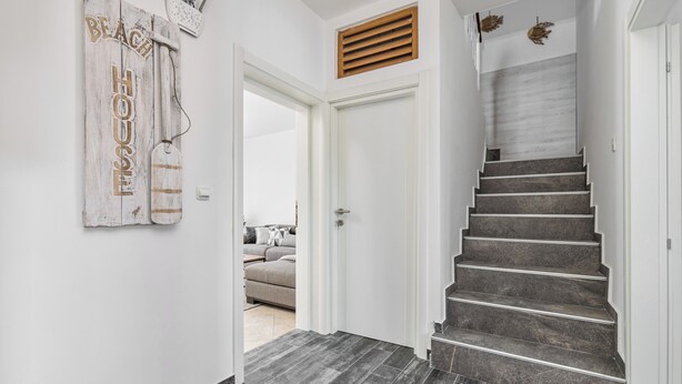 Eine Treppe mit dunklen Fliesen, eine weiße Tür und ein an der Wand befestigtes Schild mit der Aufschrift 'BEACH HOUSE'.