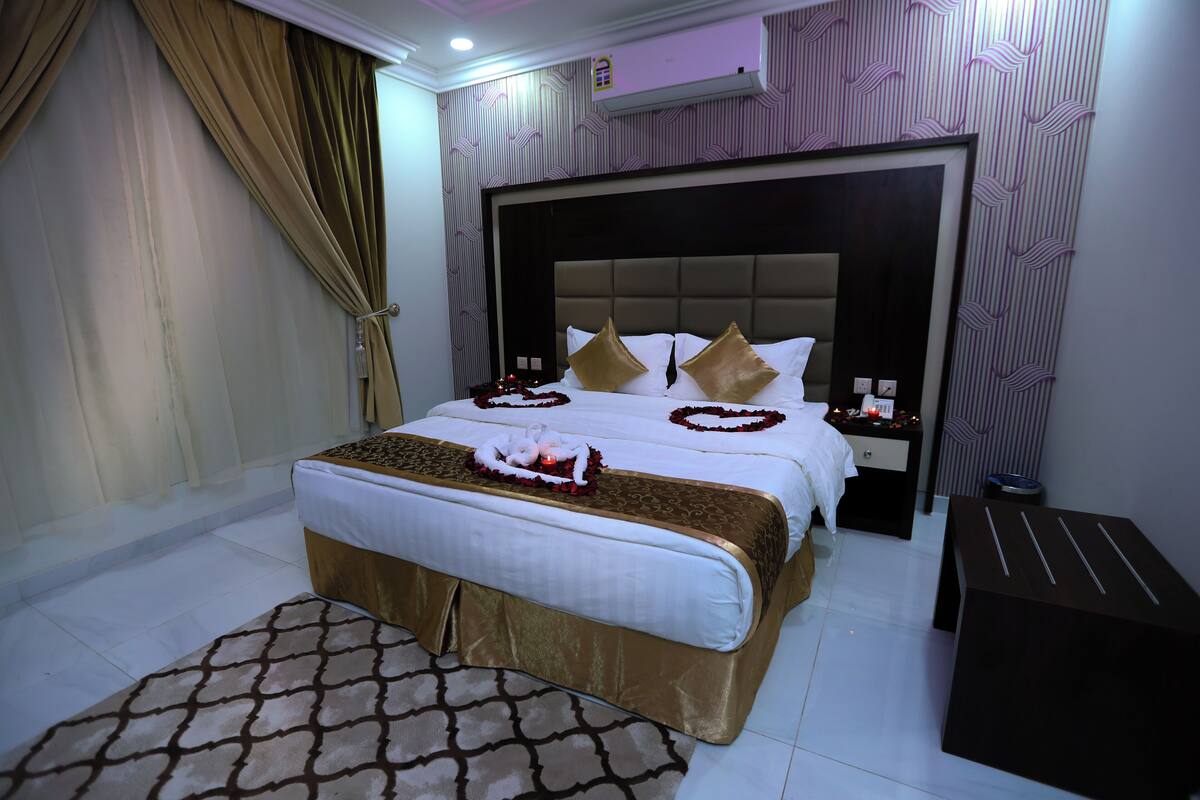 A hotel room with a large bed, a bedside table, a nightstand, and a small table.