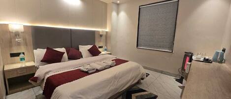 A modern hotel room with a large bed, bedside tables, a desk, and a computer.