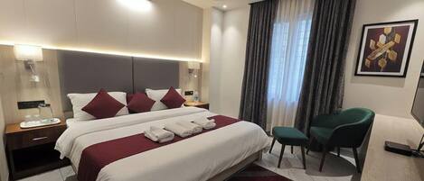 Een hotelkamer met een groot bed, nachtkastjes, een bureau, een stoel en een raam met gordijnen.