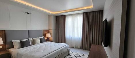 A modern hotel room with a large bed, bedside tables with lamps, a flat-screen TV, and a large window with curtains.