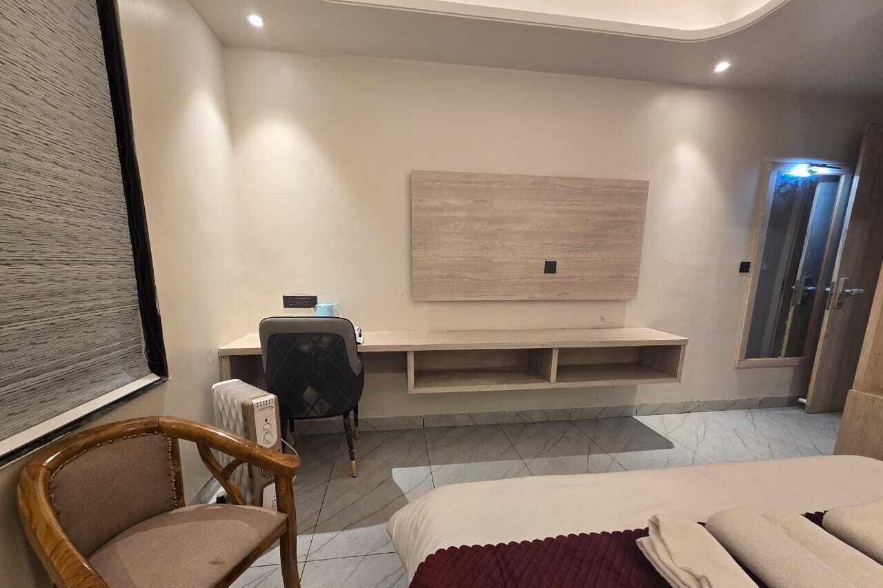 Ein modernes Hotelzimmer mit einem Bett, einem Schreibtisch, einem Sessel, einem an der Wand befestigten Fernseher und einem Duschbereich.