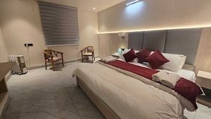 Ein modernes Hotelzimmer mit einem großen Bett, zwei Stühlen, einem Nachttisch und einem Fenster mit Jalousien.