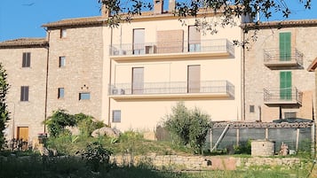 Un edificio de varios pisos con muros de piedra, balcones y un jardín.