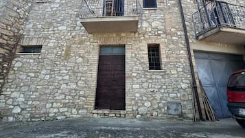 Un edificio in pietra con un ingresso centrale, un piccolo balcone con ringhiere e un'auto parcheggiata sullo sfondo.