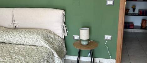 Un dormitorio con una cama, una mesita redonda con una lámpara y una pared verde.