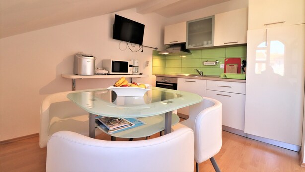 Een moderne keuken met een glazen tafel, witte stoelen, een magnetron, een broodrooster en een televisie aan de muur.
