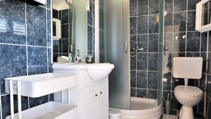 Een badkamer met douche, toilet, wastafel en een wit kastje.