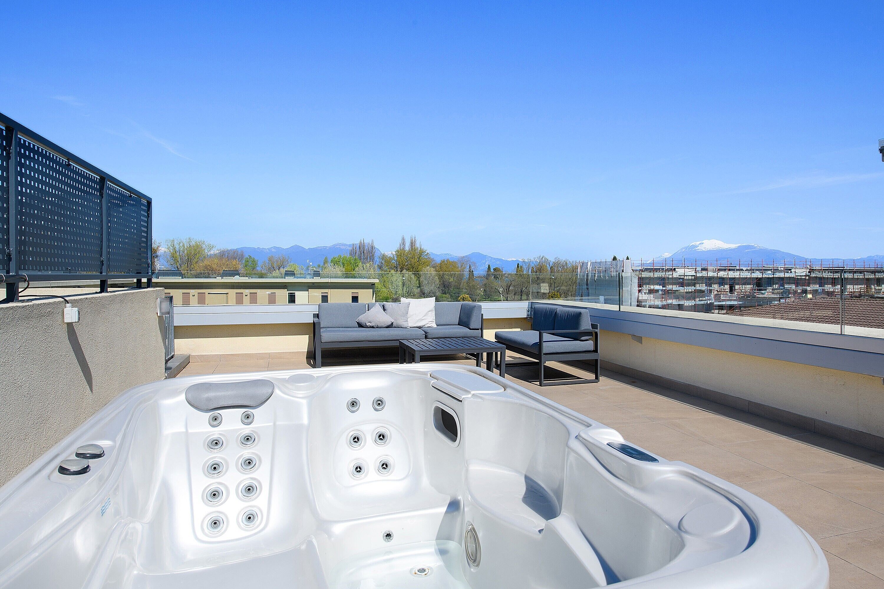 A rooftop terrace with a hot tub, outdoor seating, and a view of mountains.