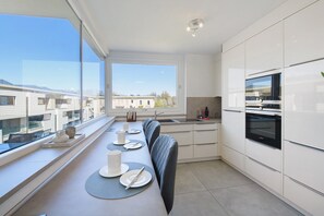 Una cocina moderna con comedor junto a un ventanal grande, que incluye un horno empotrado, un lavabo y una mesa de comedor preparada con platos y cubiertos.