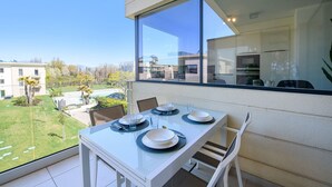 Comedor con una mesa dispuesta para cuatro, ventanas amplias y vista a una piscina y edificios.