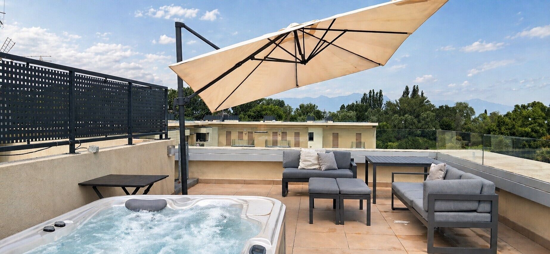 A rooftop terrace with a hot tub, outdoor furniture, and a large umbrella.