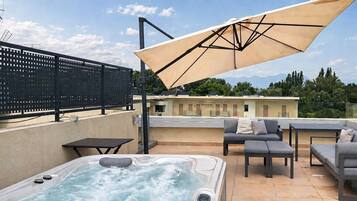 A rooftop terrace with a hot tub, outdoor furniture, and a large umbrella.