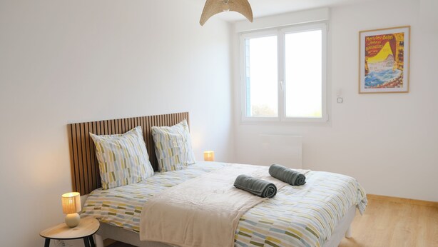 Une chambre à coucher avec un lit, des lampes de chevet, une fenêtre et une affiche accrochée au mur.
