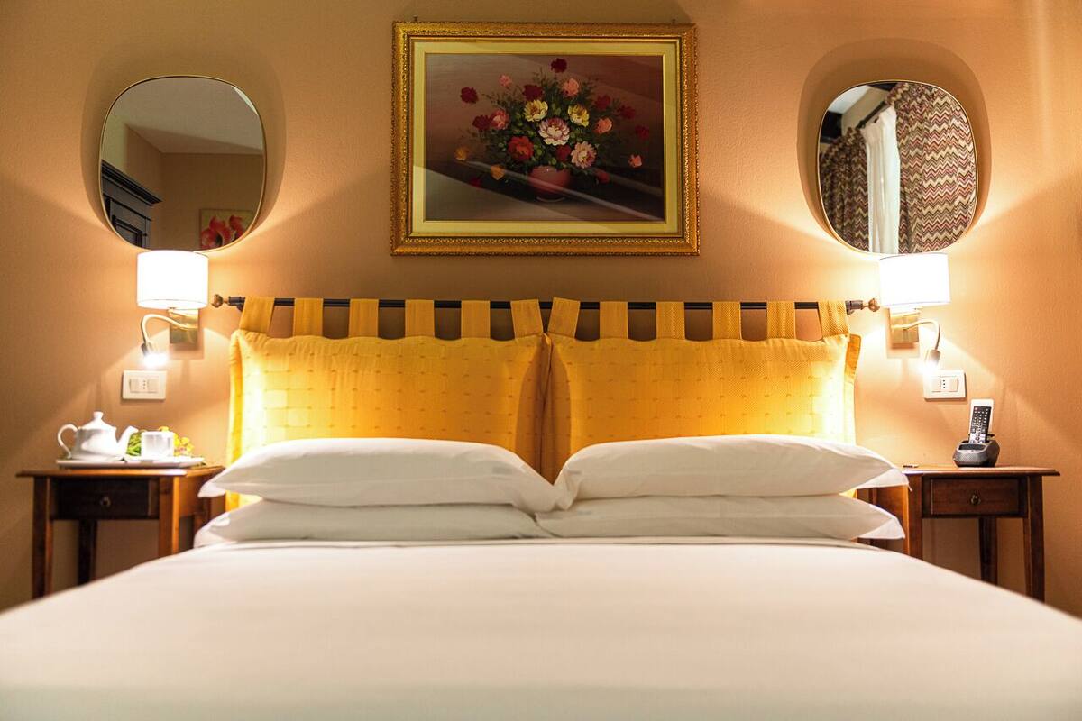 A hotel room with a bed, two bedside tables, a nightstand, a mirror, and a framed floral artwork on the wall.
