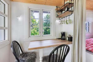A room with a wooden table, two chairs, a window with a view of greenery, and a shelf with kitchen items. - Tiny Home Waldwagen Altes Forstamt Sinntal, sep. kitchen/bath 50m, mountain view, 18k sqm garden (Sinntal)