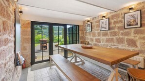 Une pièce aux murs de pierre, avec une table en bois, un banc et des tableaux encadrés accrochés au mur.