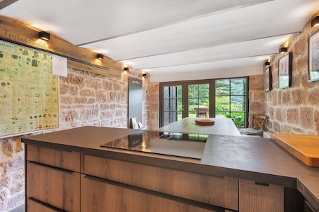A modern kitchen with a stone wall, wooden cabinets, and a large island.. Tiny Home Waldwagen Altes Forstamt Sinntal, sep. kitchen/bath 50m, mountain view, 18k sqm garden