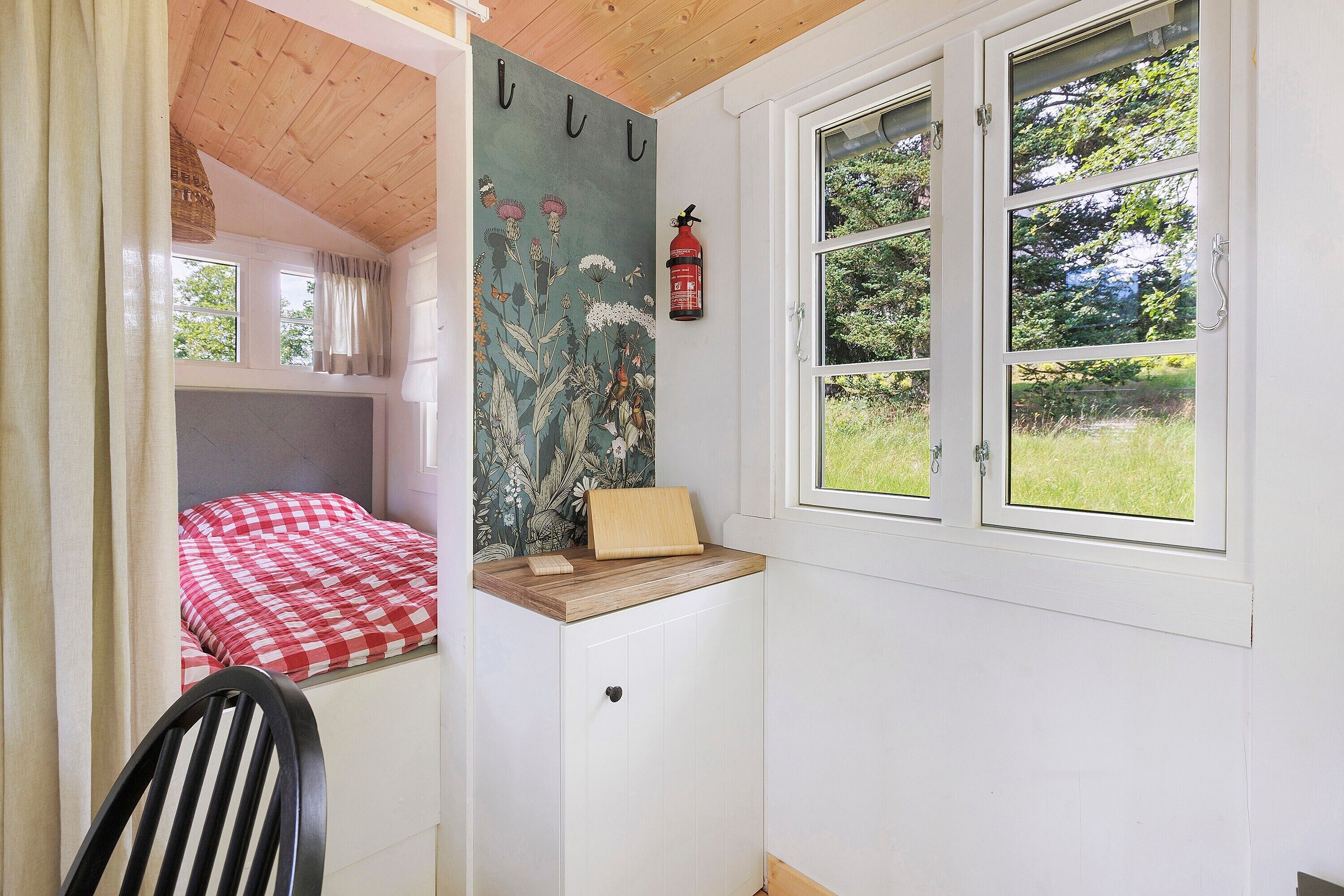 A room with a bed, a small desk, a chair, a window, and a fire extinguisher.