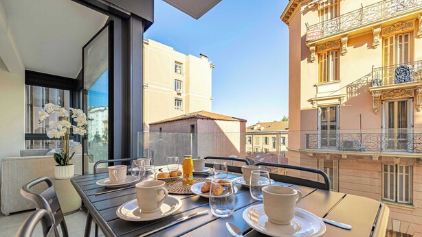 A dining table set with plates, cups, and a bottle, overlooking a cityscape. - Superb terrace apartment in Monaco-Beausoleil (Beausoleil)