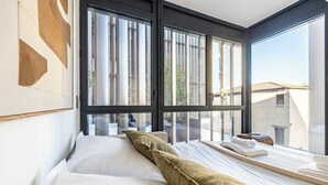 A hotel room with a bed, pillows, a window, and a view of buildings outside. - Superb terrace apartment in Monaco-Beausoleil (Beausoleil)