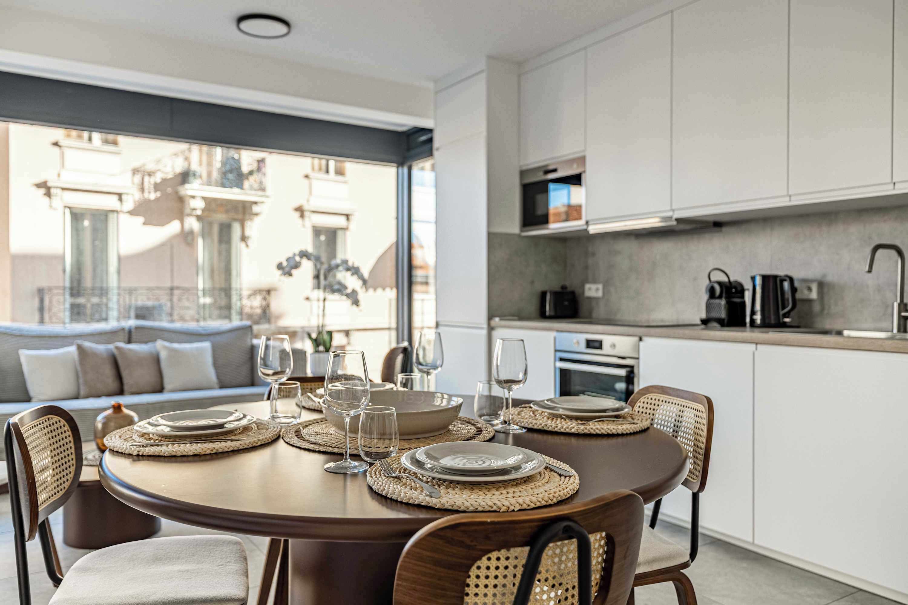 Een moderne eetruimte met een ronde tafel gedekt voor vier personen, omringd door rieten stoelen.