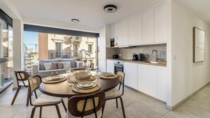 A modern kitchen with white cabinets, a dining area with a round table and chairs, and a view of a balcony with outdoor furniture. - Superb terrace apartment in Monaco-Beausoleil (Beausoleil)