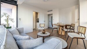 En moderne stue med sofa, stole, spisebord og et køkken, der kan ses gennem en åben dør.
