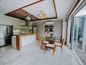 A modern kitchen with a central island, stainless steel appliances, and a dining area with a glass table and wooden chairs. - Luxury Private Villa Pool & Jacuzzi Juan Dolio (Guayacanes)