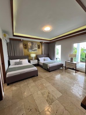 A hotel room with two beds, a ceiling light, a nightstand with a lamp, a wall art piece, and a window with a view. - Luxury Private Villa Pool & Jacuzzi Juan Dolio (Guayacanes)