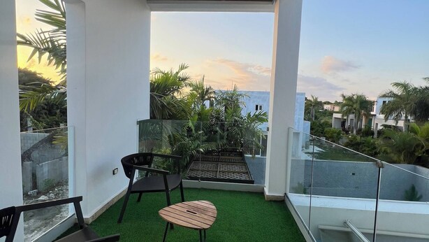 En balkon med kunstgræs, to stole, et lille bord og udsigt til et boligområde.
