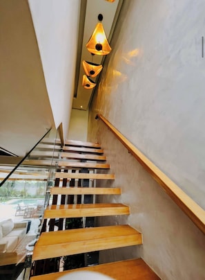 Un escalier moderne avec des marches en bois et une rampe en verre, menant à une pièce offrant une vue sur un espace extérieur.