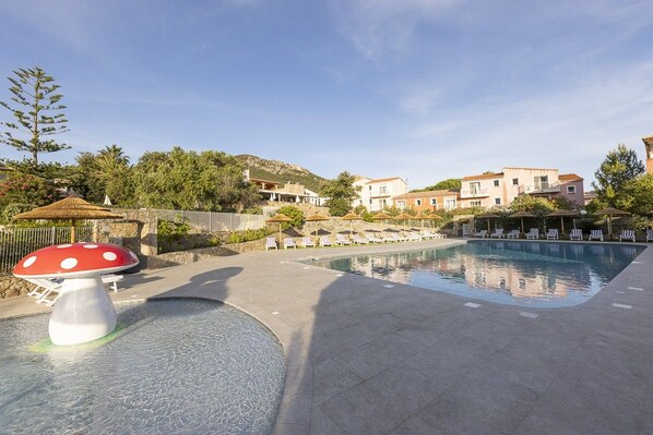 A swimming pool area with lounge chairs and a mushroom-shaped fountain.