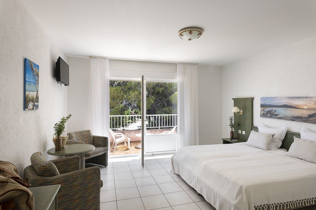 Habitación de hotel con cama, sofá, una mesita, televisor y balcón con mobiliario exterior.