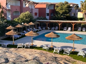 A poolside area with lounge chairs and umbrellas, a swimming pool, and a building with balconies. - Hôtel Maristella (Aregno)