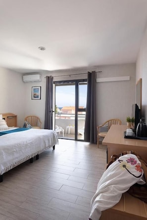 A hotel room with a bed, a desk, a chair, a balcony, and a view of the outside. - Hôtel Maristella (Aregno)