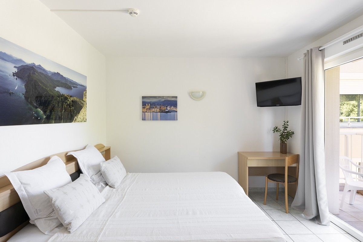 Een slaapkamer met een groot bed, een bureau, een stoel, een televisie en een raam met gordijnen.